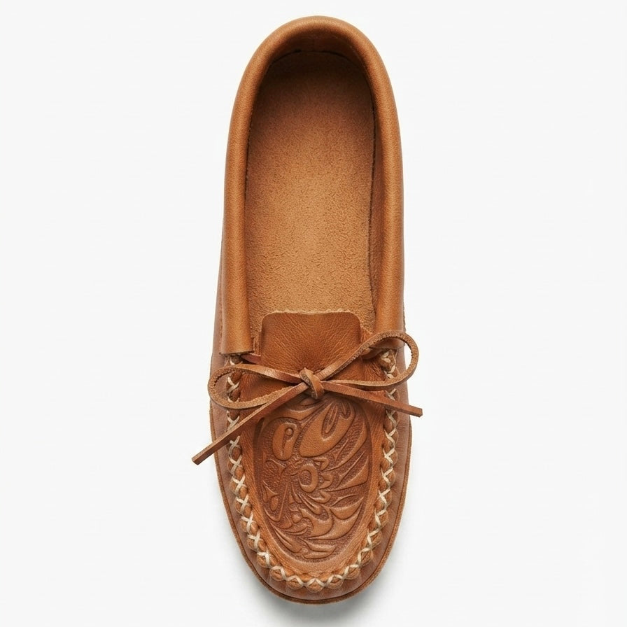 A single tan leather moccasin loafer shown from a top-down view on a light gray background. The shoe features hand-tooled floral detailing on the vamp, a matching leather tie bow, and whipstitching around the edge.