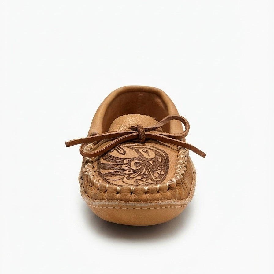 A single tan leather moccasin-style baby shoe with a decorative brown embroidered design on the toe and a matching brown bow on the upper, shown against a plain white background.
