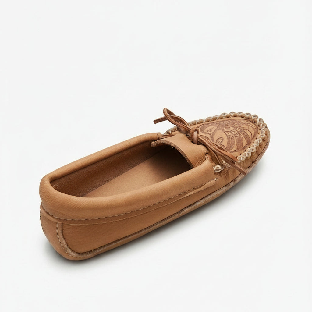 A single tan leather moccasin loafer shown from a three-quarters angle on a light gray background. The shoe features a tan leather upper, a braided jute trim around the toe, a decorative embroidered pattern on the vamp, and a matching tan leather tie-moccasin bow.